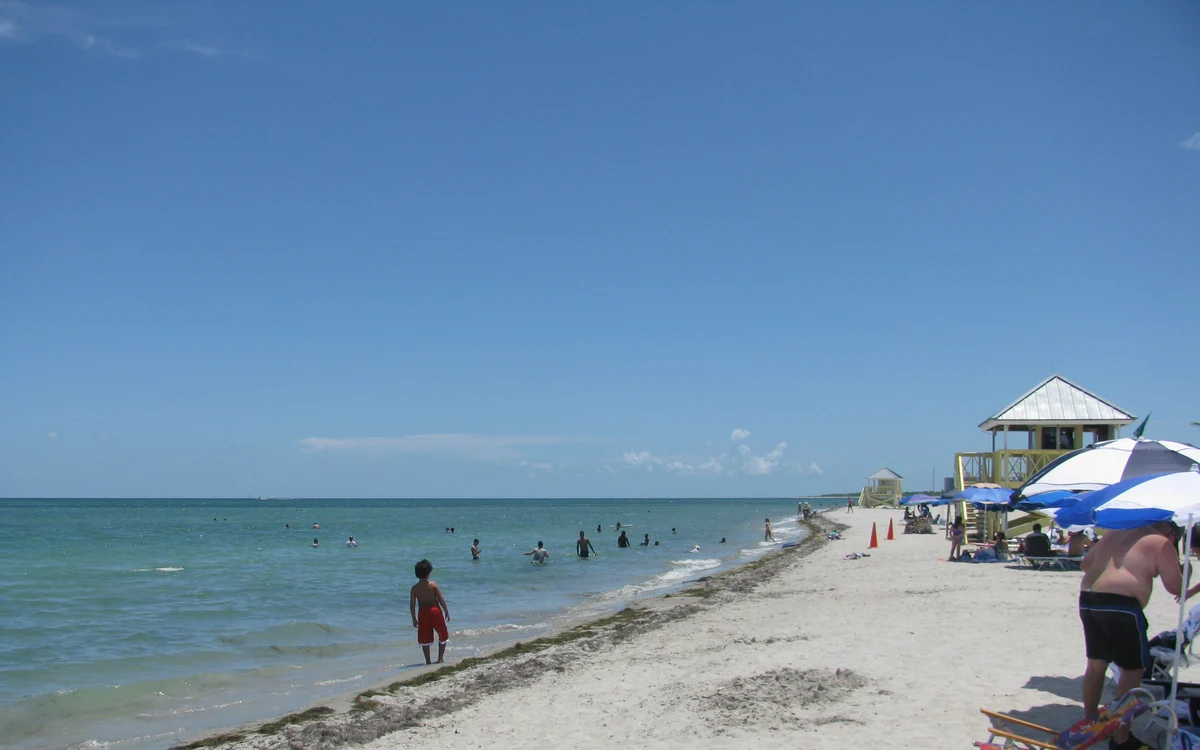 Swimmers in the shallow water at Crandon Park Beach, with the park's yellow and white lifeguard cabanas along the sand