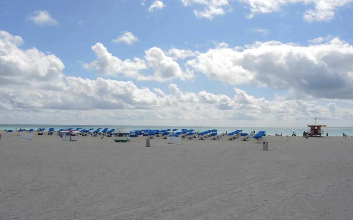 Rows of blue parasols and beach cabanas on the sand at Lummus Park Beach, with a pink Art Deco lifeguard tower to the right