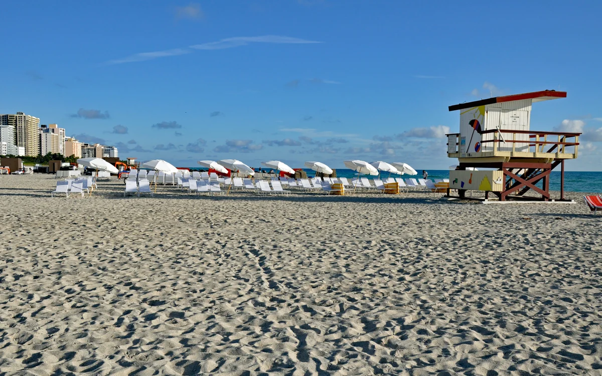 Early morning on Miami Beach: a rank of white parasols and loungers set out on the sand beside a lifeguard tower