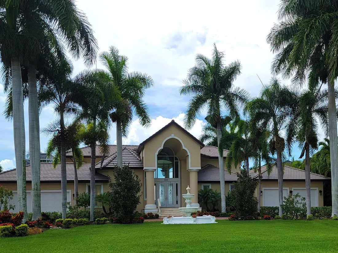 A Florida house behind palms with a green lawn and a fountain