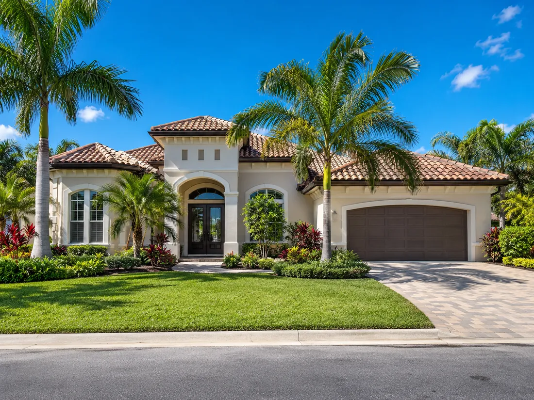A finished single story Florida house with a barrel tile roof, an arched entry, a paver driveway and palms across the front
