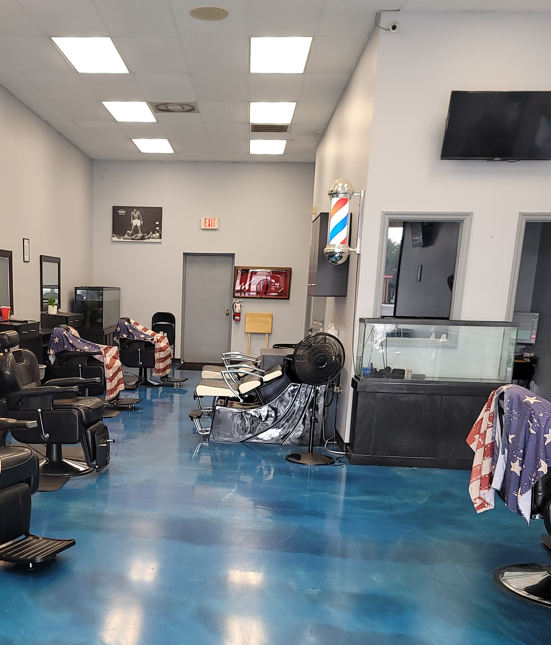 Inside Rich City Barber: black barber chairs under flag-print capes, a blue floor, a barber pole on the wall and a boxing photograph on the back wall
